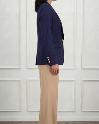 Woman side view wearing a navy blazer with one button in the front and beige trousers